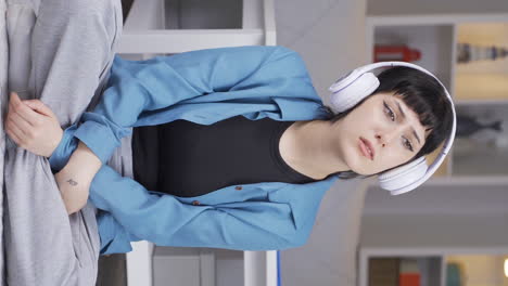 Vertical-video-of-Young-woman-listening-to-music-with-headphones-is-unhappy-and-sad.